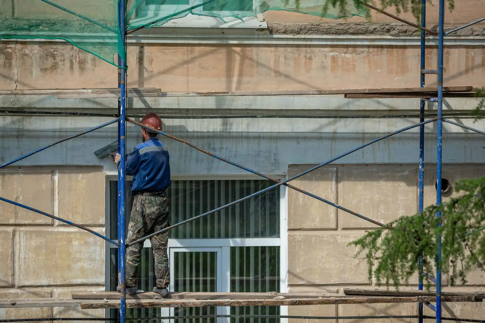 Handwerker mit Helm auf einem Gerüst bei Arbeiten an einer Gebäudefassade