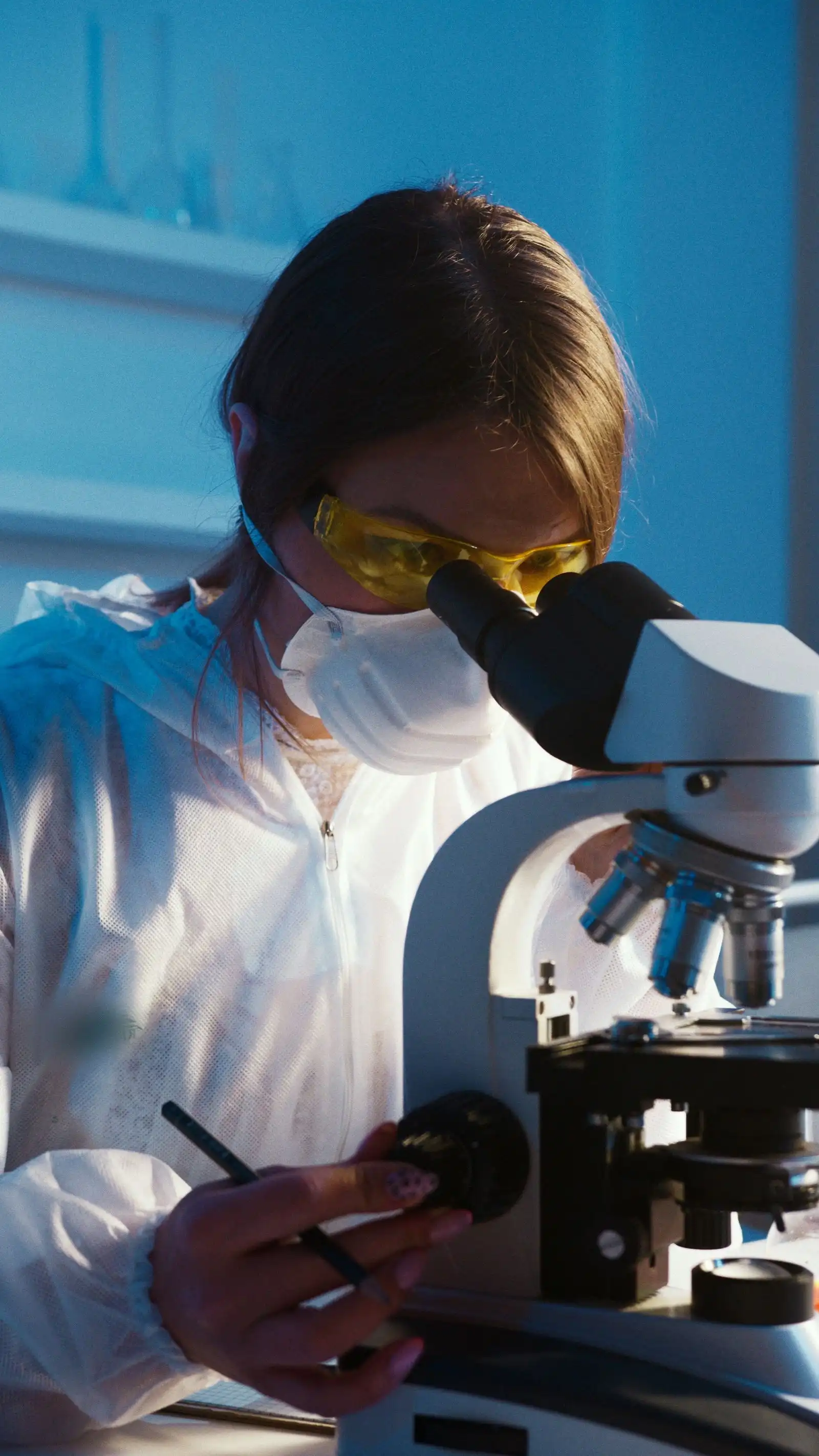Luftanalysen & Freimessung VDI 3492 in Minden – Laborfachkraft mit Schutzbrille und Maske bei der Schadstoff-Probenauswertung am Mikroskop