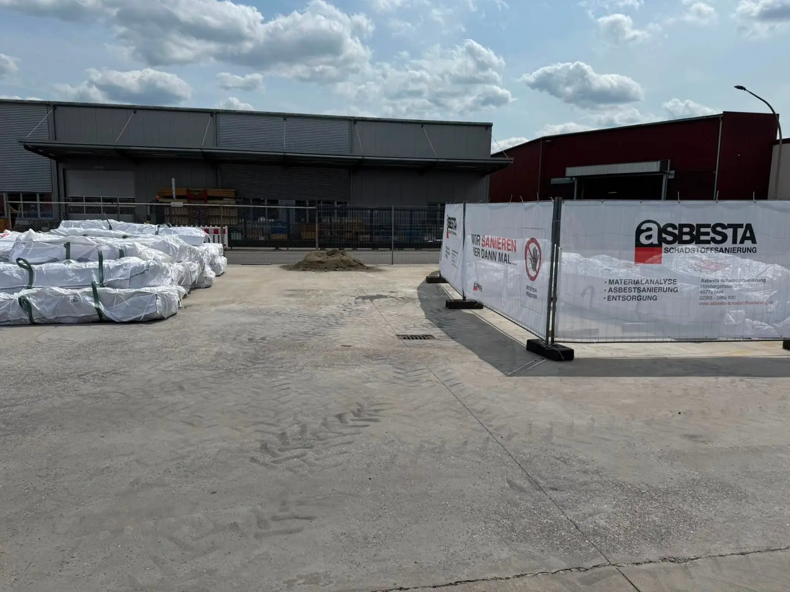 Betriebsgelände von Asbesta in Marl mit verpackten Big-Bags und Bauzaun-Banner „Asbesta Schadstoffsanierung"