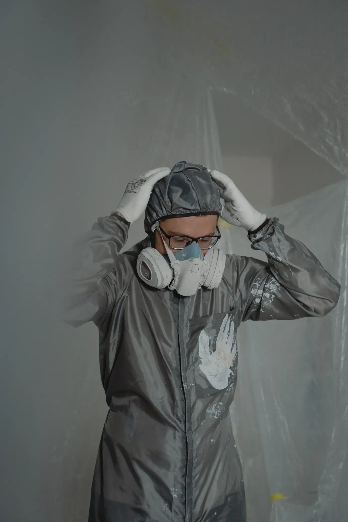 Fachkraft mit Atemschutz-Halbmaske, Schutzbrille und Schutzanzug vor Staubschutzfolie bei der Schadstoffsanierung